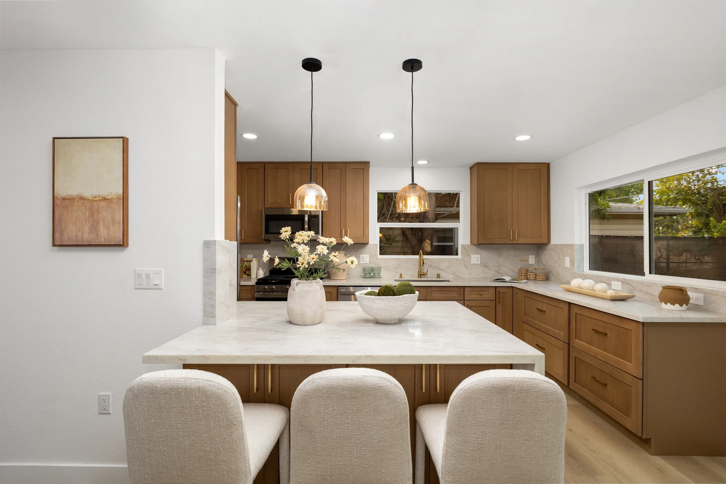 A kitchen island lit by two warm glass pendants, windows beyond